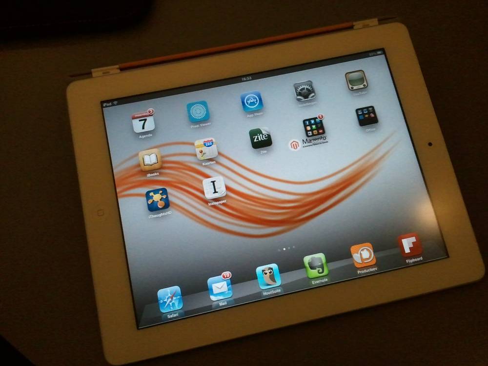 An iPad home screen shows app icons over an orange flowing Magento wallpaper.