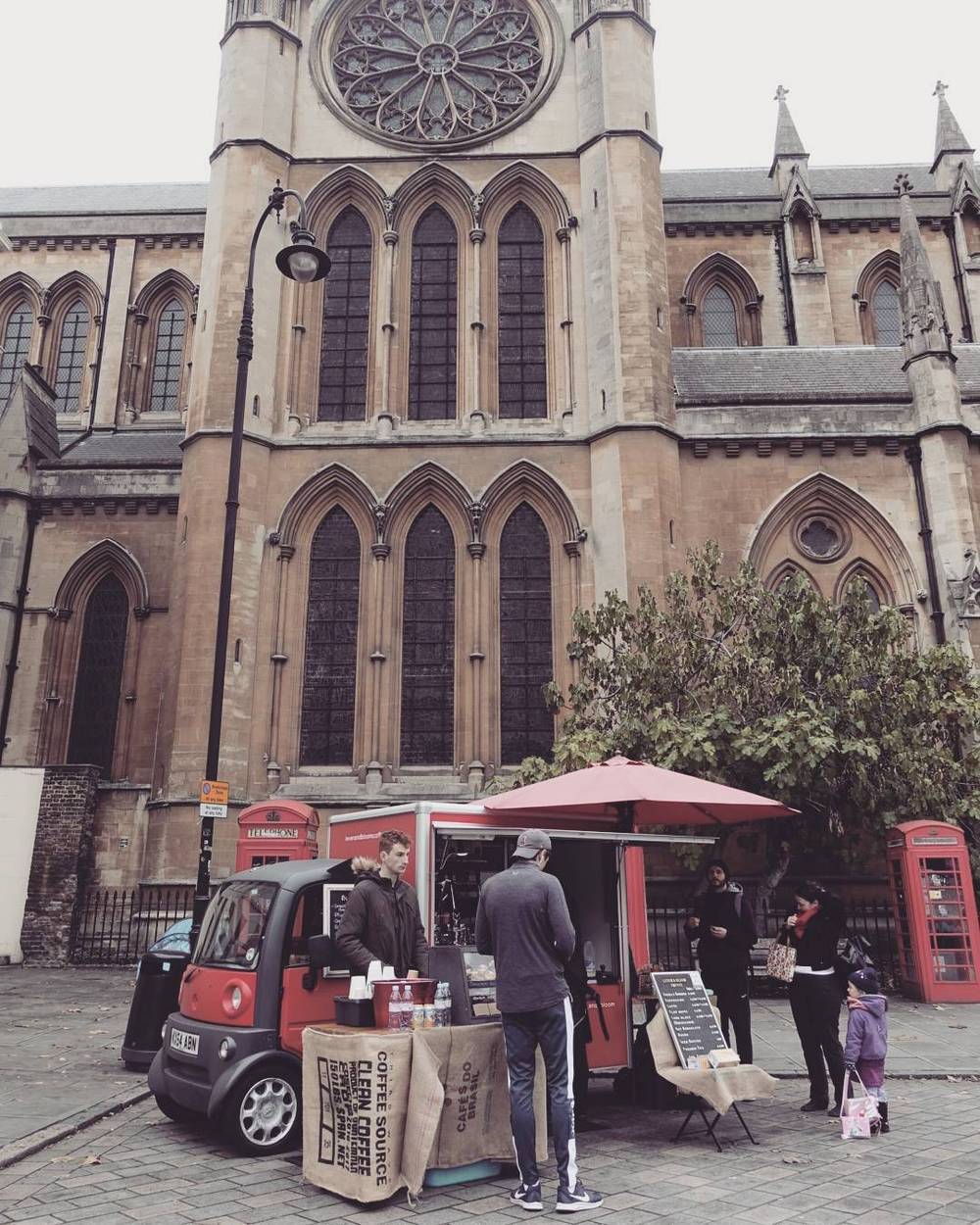 A London street scene with a red telephone box and a small food stall outside a historic church.