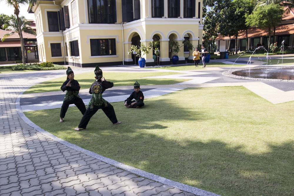 Performers in black costumes practice martial arts on a lawn near a heritage building.