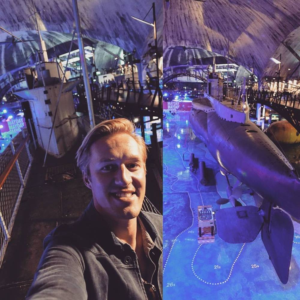 Selfie in front of a submarine and diving equipment displayed in a purple-lit museum hall.