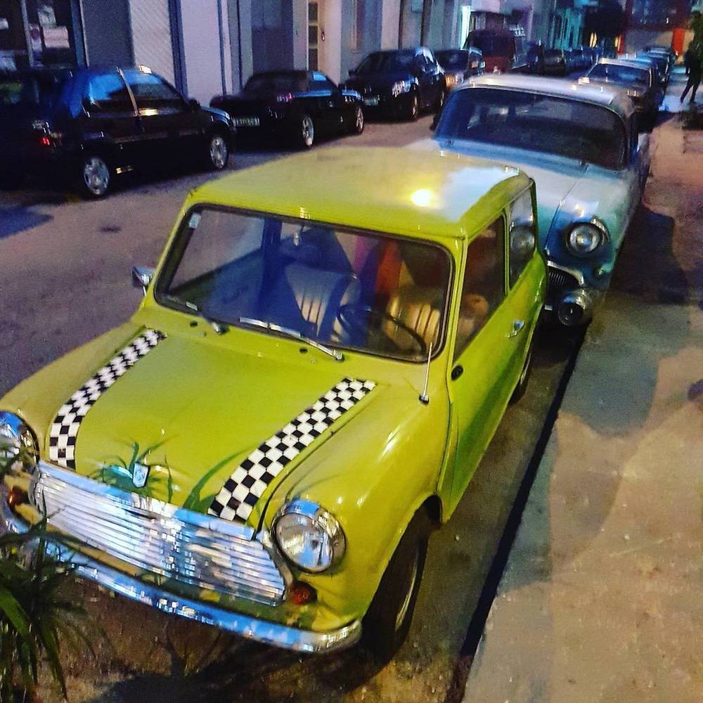 Vintage cars, including a bright yellow one, parked along a street at dusk.