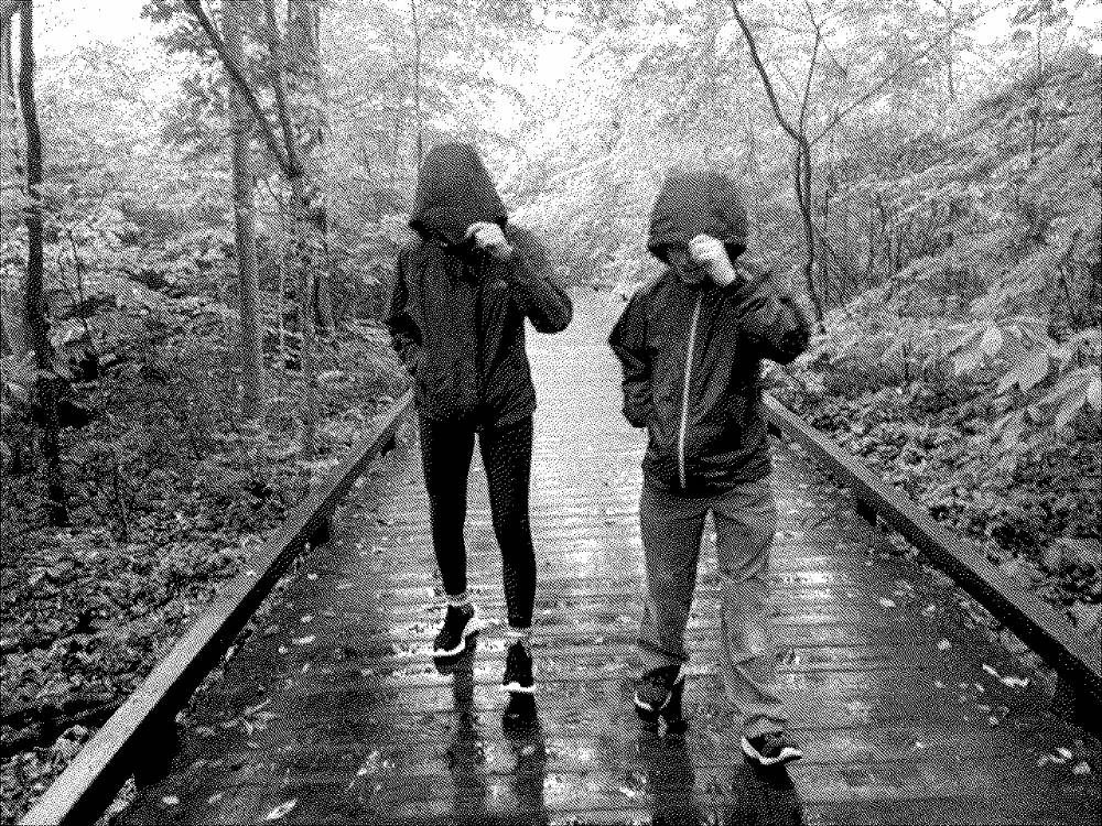 two children pulling raincoat hoods down as they lean into the rain