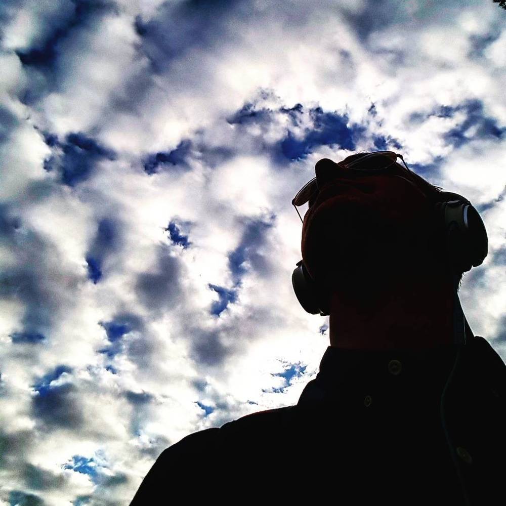 Silhouette of a person wearing headphones against a sky of scattered clouds.