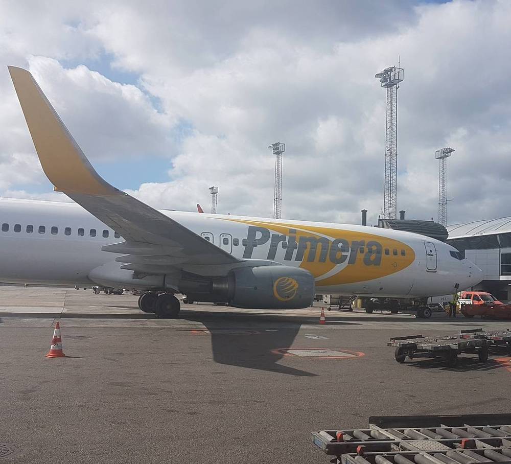 A white Primera Air passenger jet parked on the tarmac under a cloudy sky.