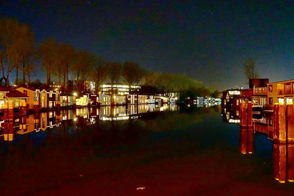 Waterside houses and boats reflected in a calm canal at dusk.