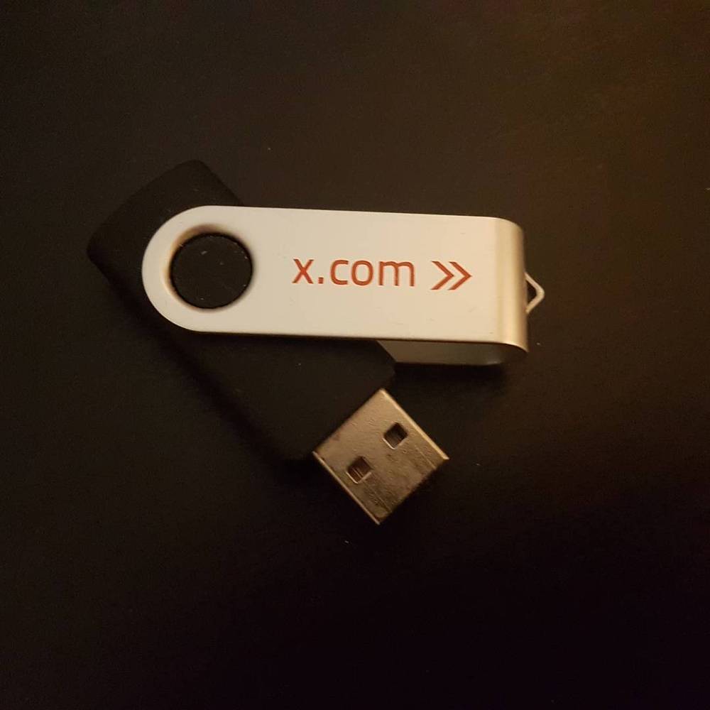 A USB flash drive printed with "x.com" on a dark surface.