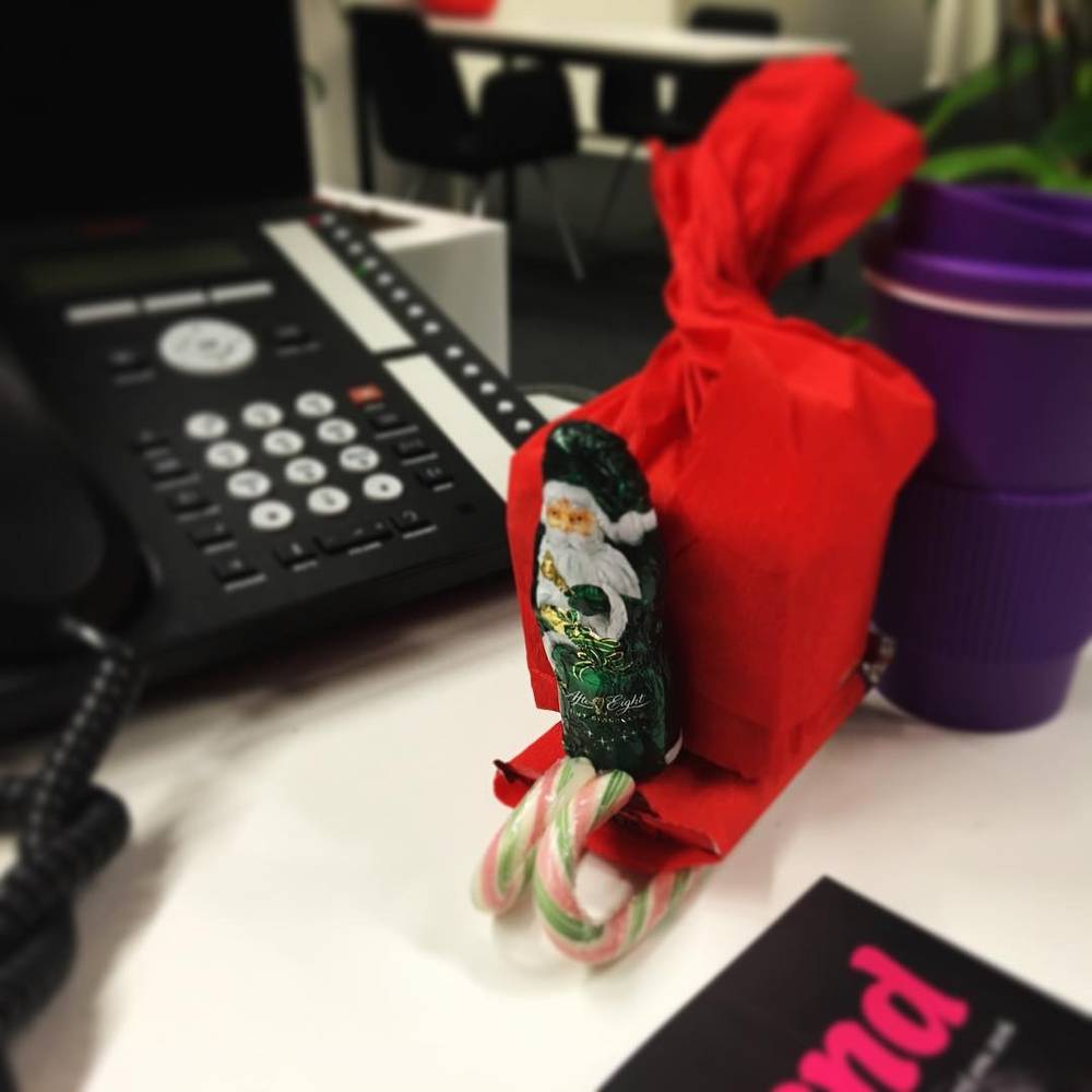 An office phone beside a small red gift bag decorated with a Santa figure and candy canes.