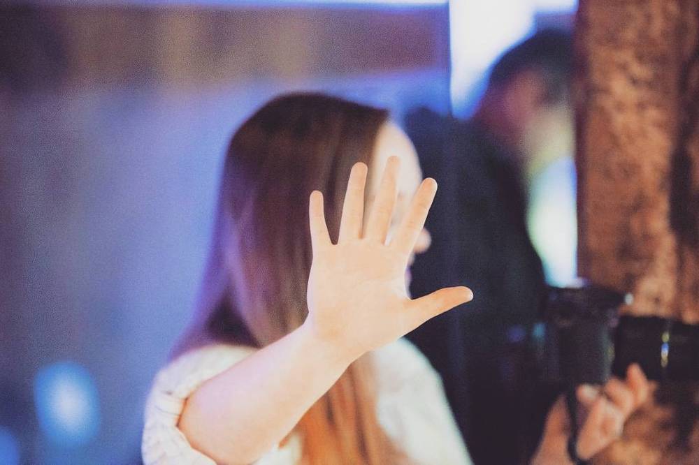 A woman raises her hand toward the camera in a motion-blurred, backlit shot.