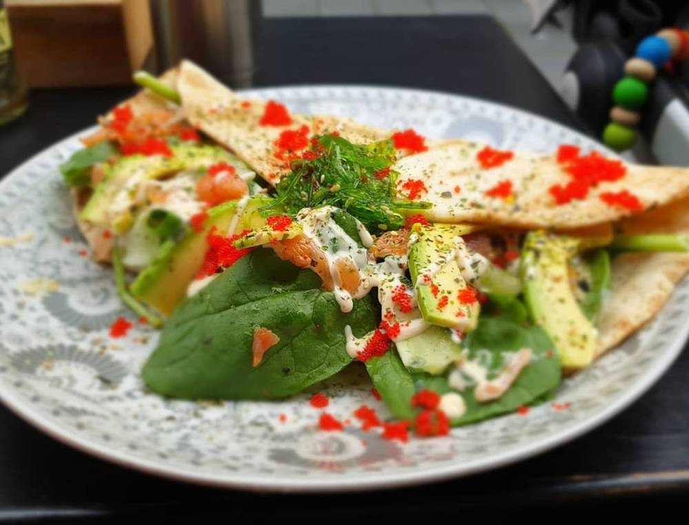 A plated wrap with salad greens, avocado, tomato and roe garnish.