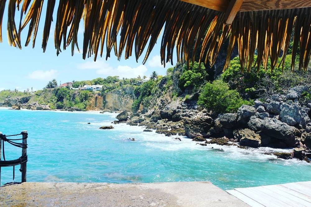 View of a rocky turquoise cove seen from beneath a thatched roof.