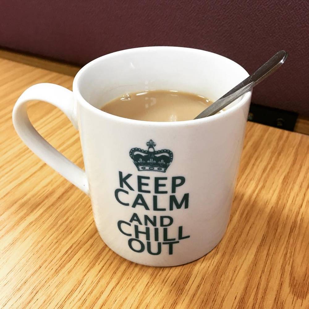 A mug reading "Keep Calm and Chill Out" filled with tea on a wooden desk.