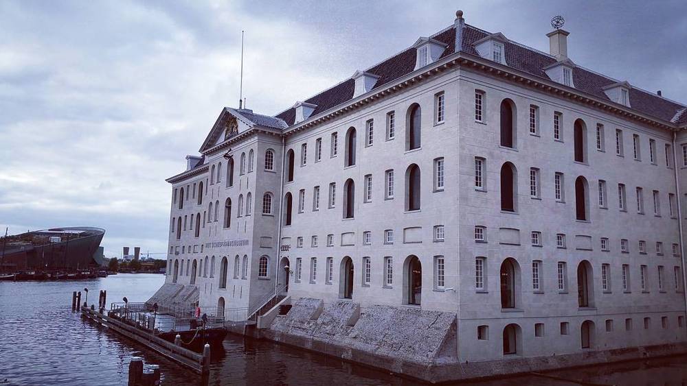 A stately white stone building with rows of arched windows, seen from across the water.