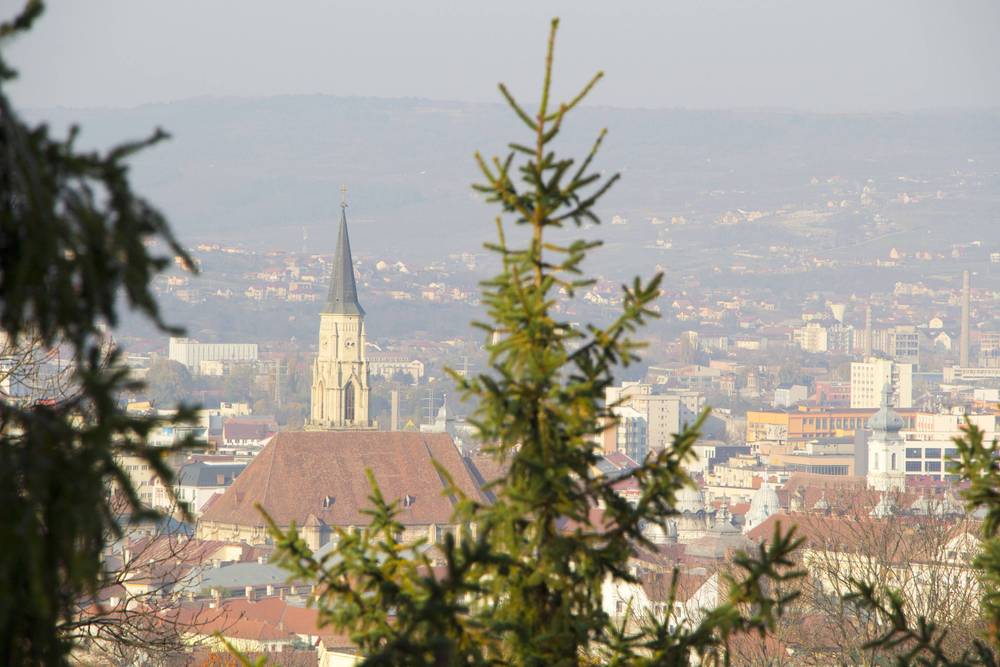 A hilltop view over Cluj-Napoca with a church spire in the foreground.