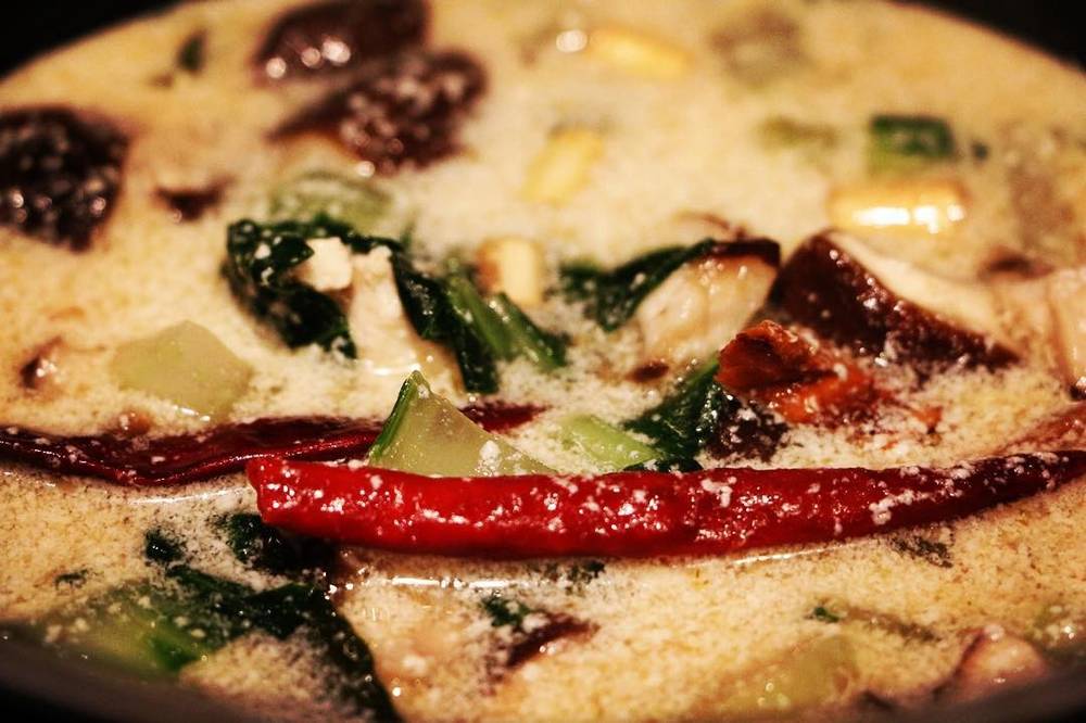 A close-up of Thai tom kha soup with chili peppers and greens.