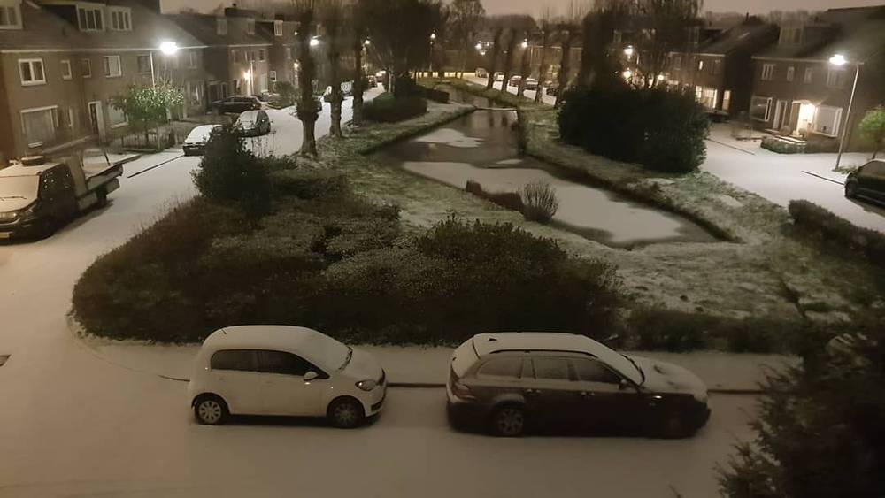 A snowy residential street at night with parked cars and houses.