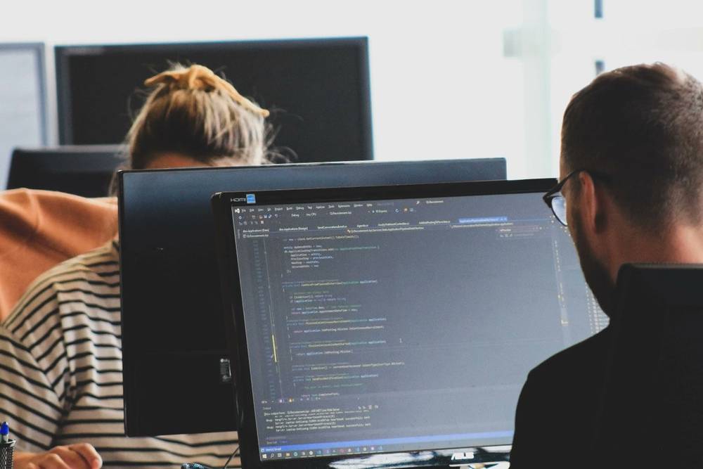 Two colleagues looking at code on computer monitors in an office.