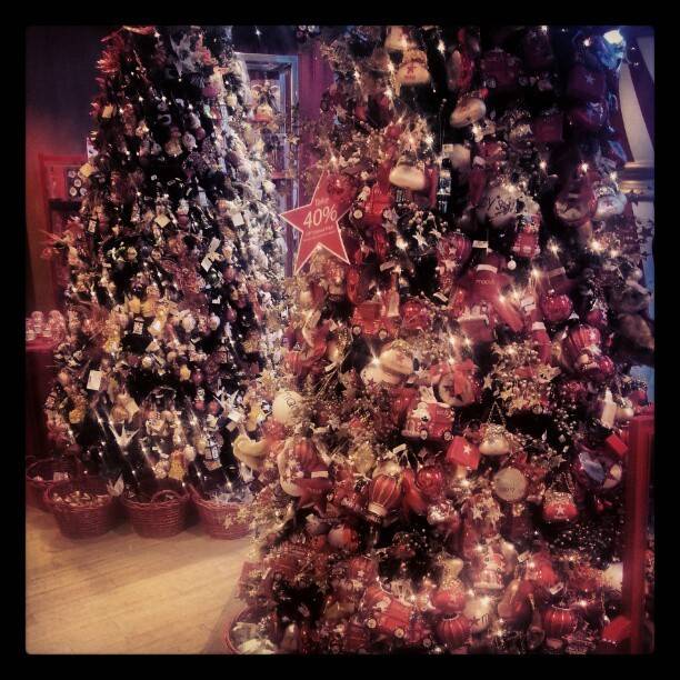 A Christmas tree densely decorated with red and gold ornaments and a sale sign in a shop.