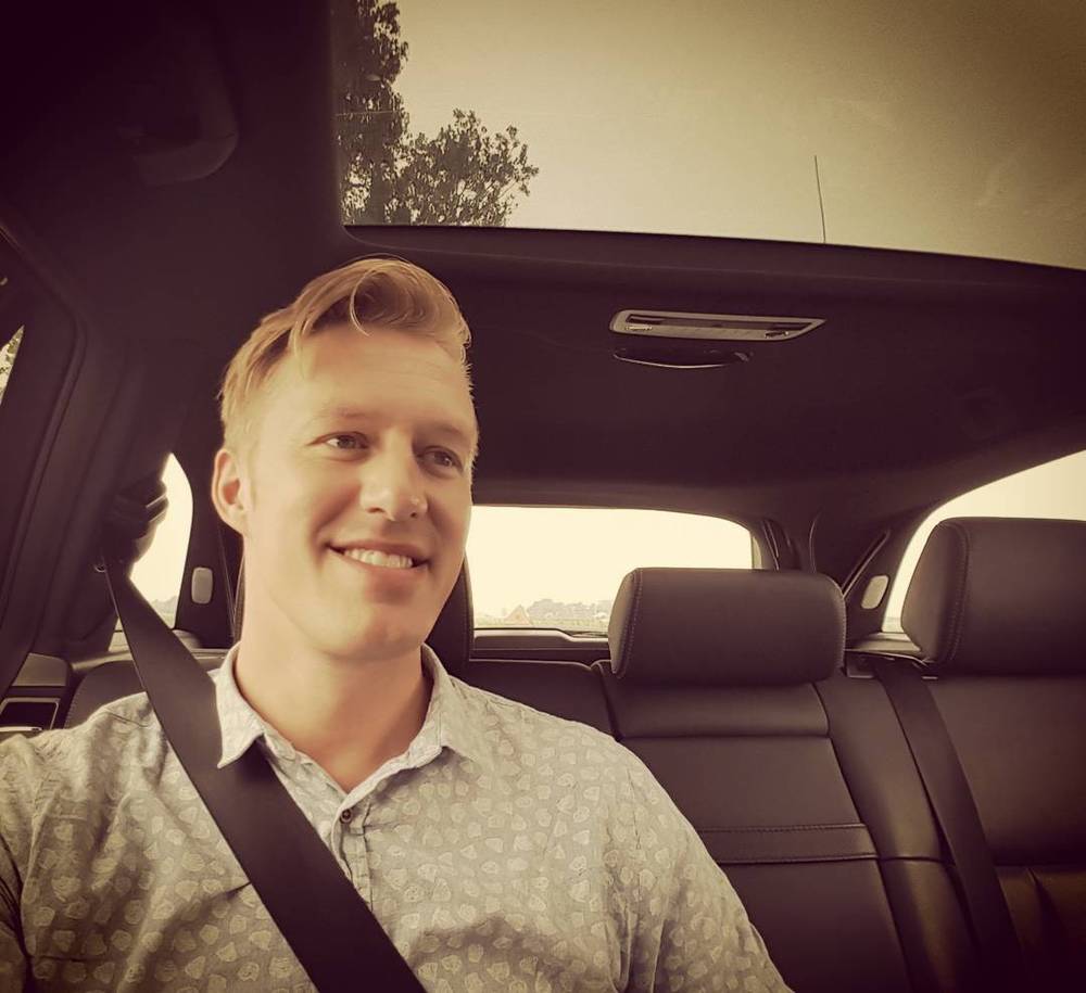 Selfie of a man smiling while seated in a car with a sunroof.