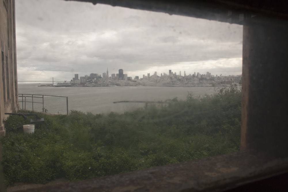 The San Francisco skyline is seen hazily through a barred Alcatraz window.