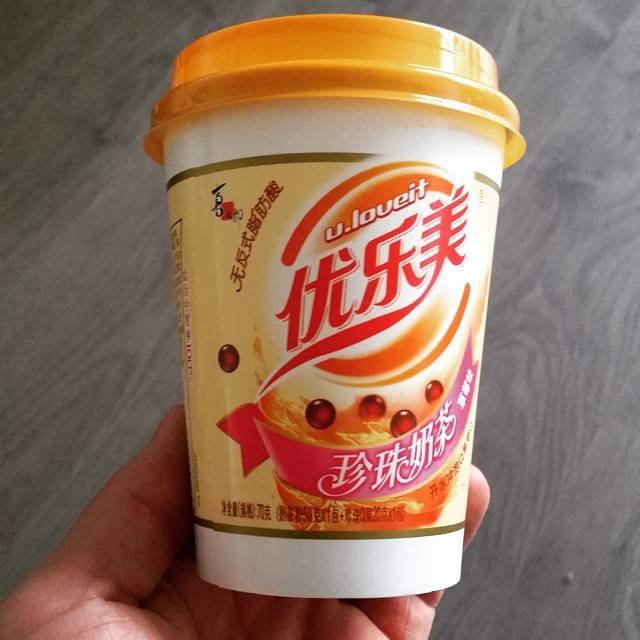 A hand holds a cup of bubble tea with Chinese branding on the packaging.