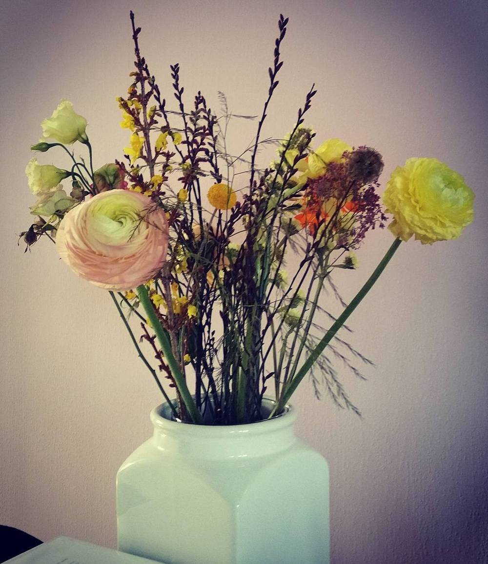 A small bouquet of pink and yellow flowers in a white glass vase.