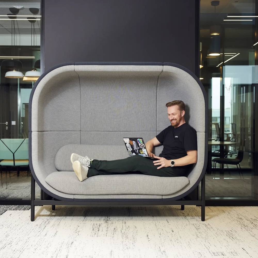 A man reclining with a laptop in a large enclosed pod-style office chair.