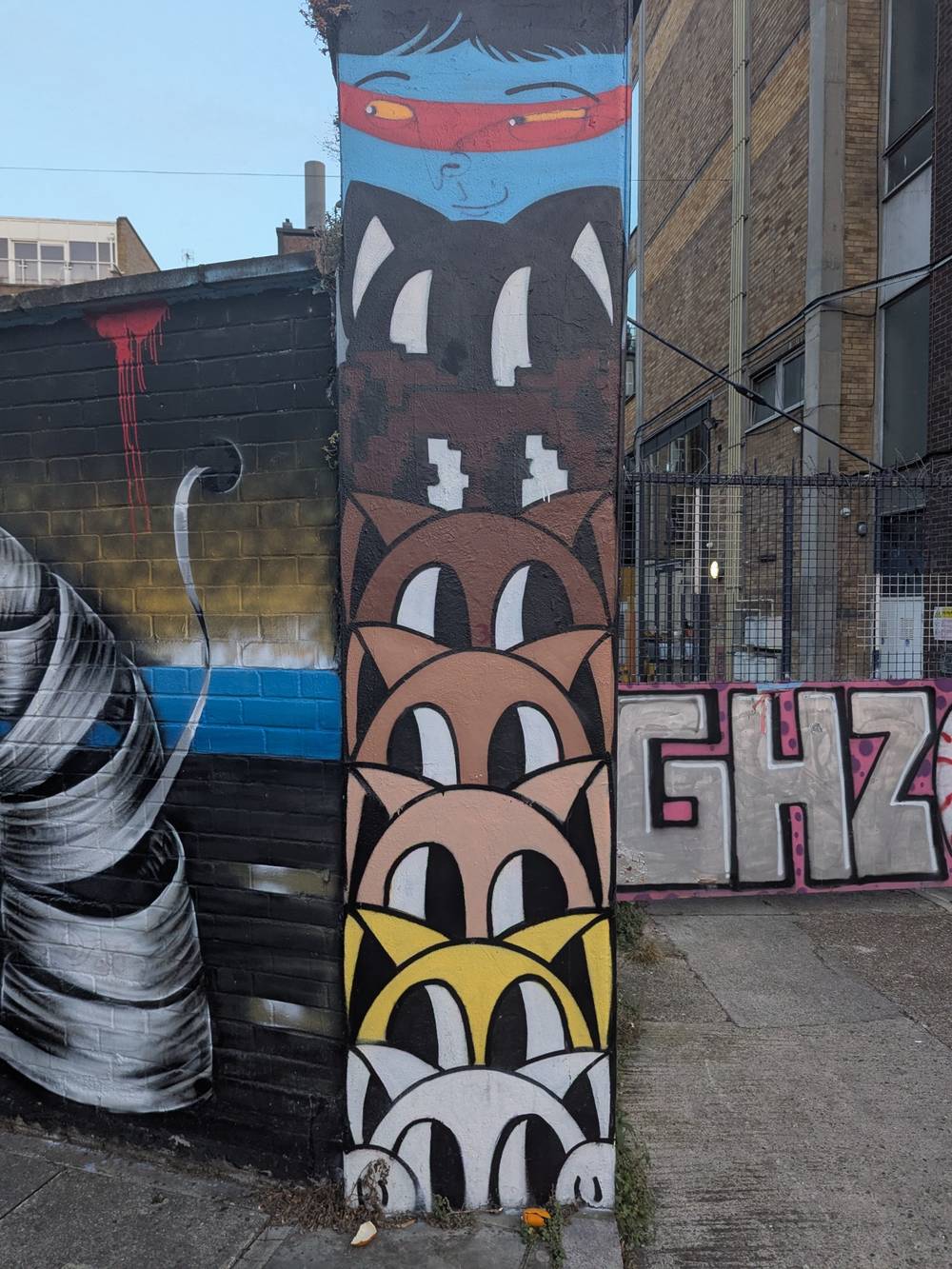 Micho Gato section of Hanbury Street Collab. 7 cat faces in Gato's distinctive style stacked in a white-to-black gradient. A blue and red face by Cranio crowns the stack of cats.