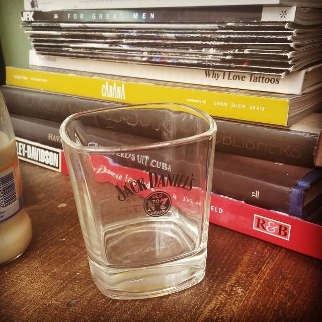 An empty Jack Daniel's whiskey glass on a wooden shelf next to a stack of books.