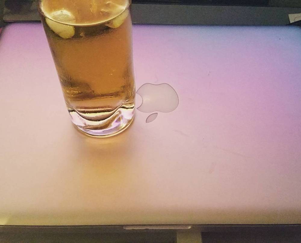 A glass of iced tea on a laptop with a spilled drop next to the Apple logo.