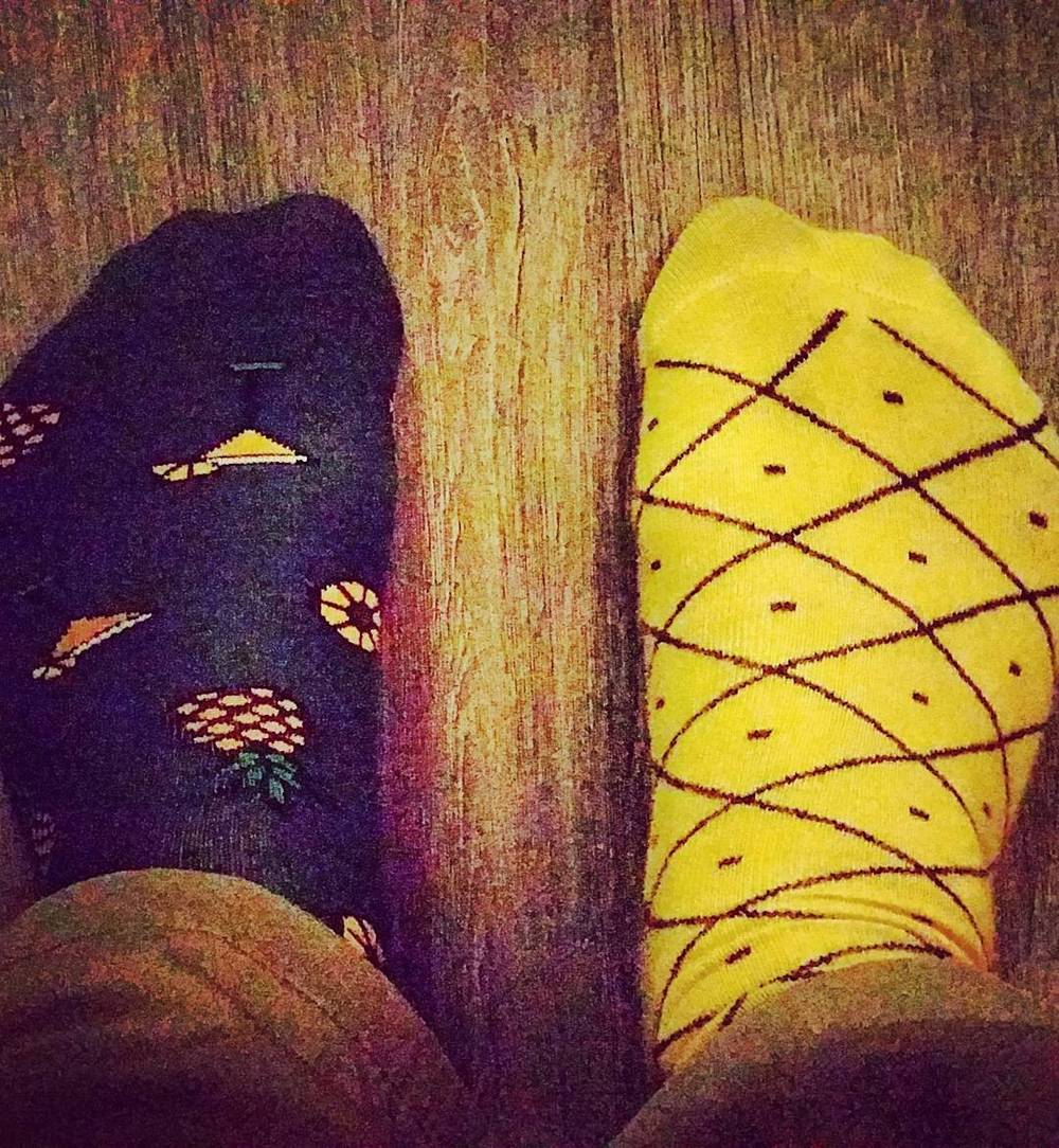 Two feet propped up wearing a dark patterned sock and a yellow diamond-patterned sock.