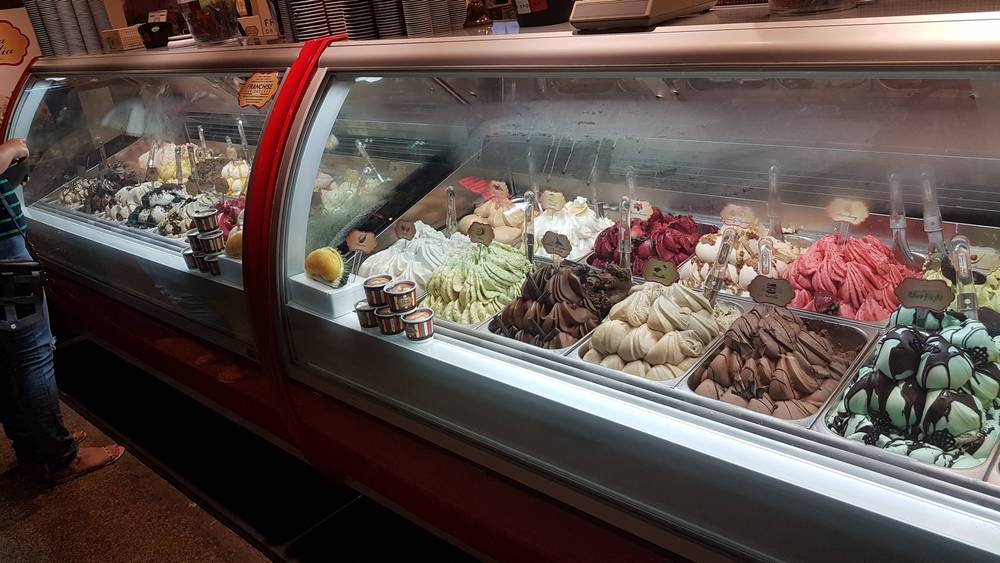 A gelato display case is filled with colorful flavors.