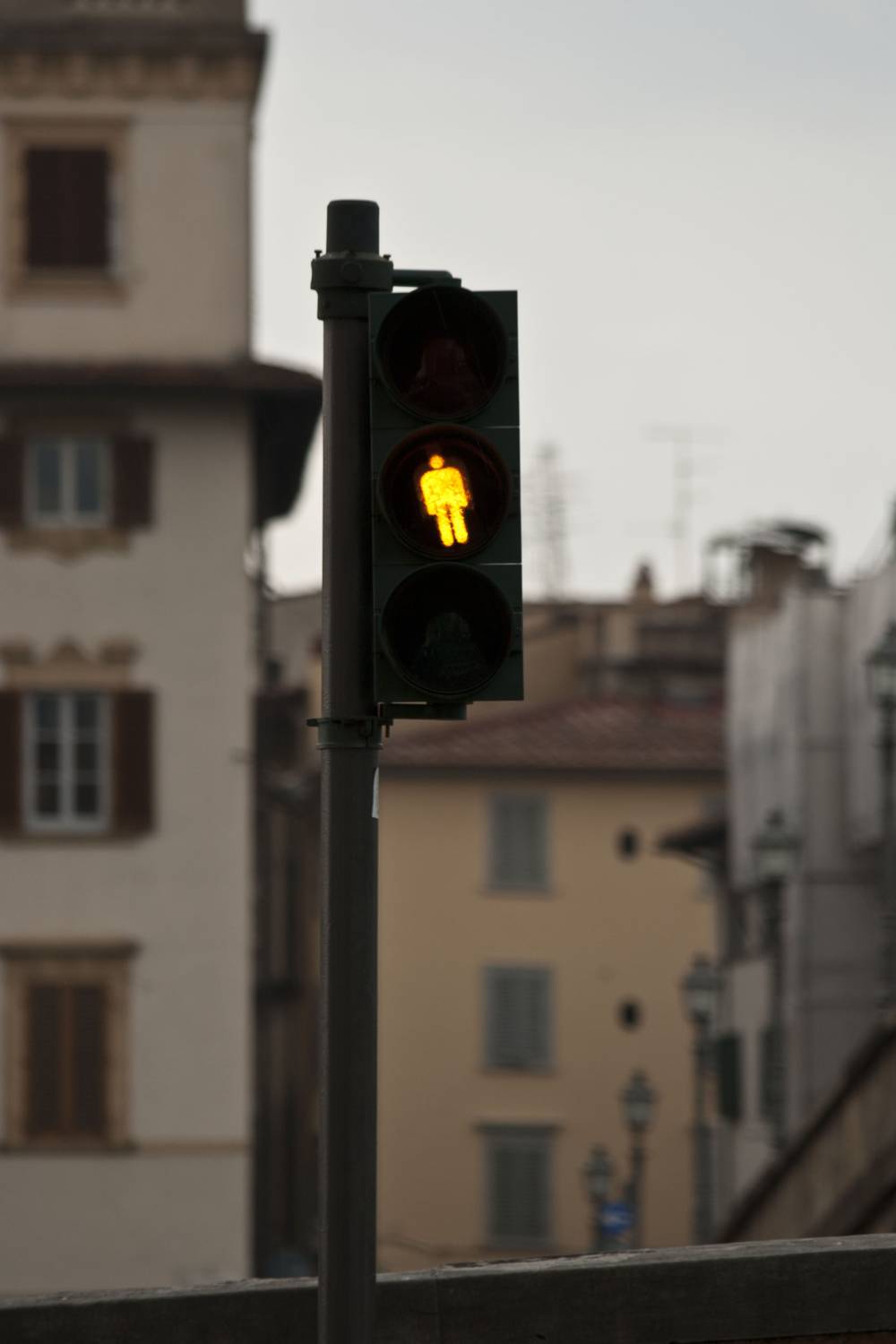 A pedestrian traffic light shows a walking figure against a row of shuttered buildings.