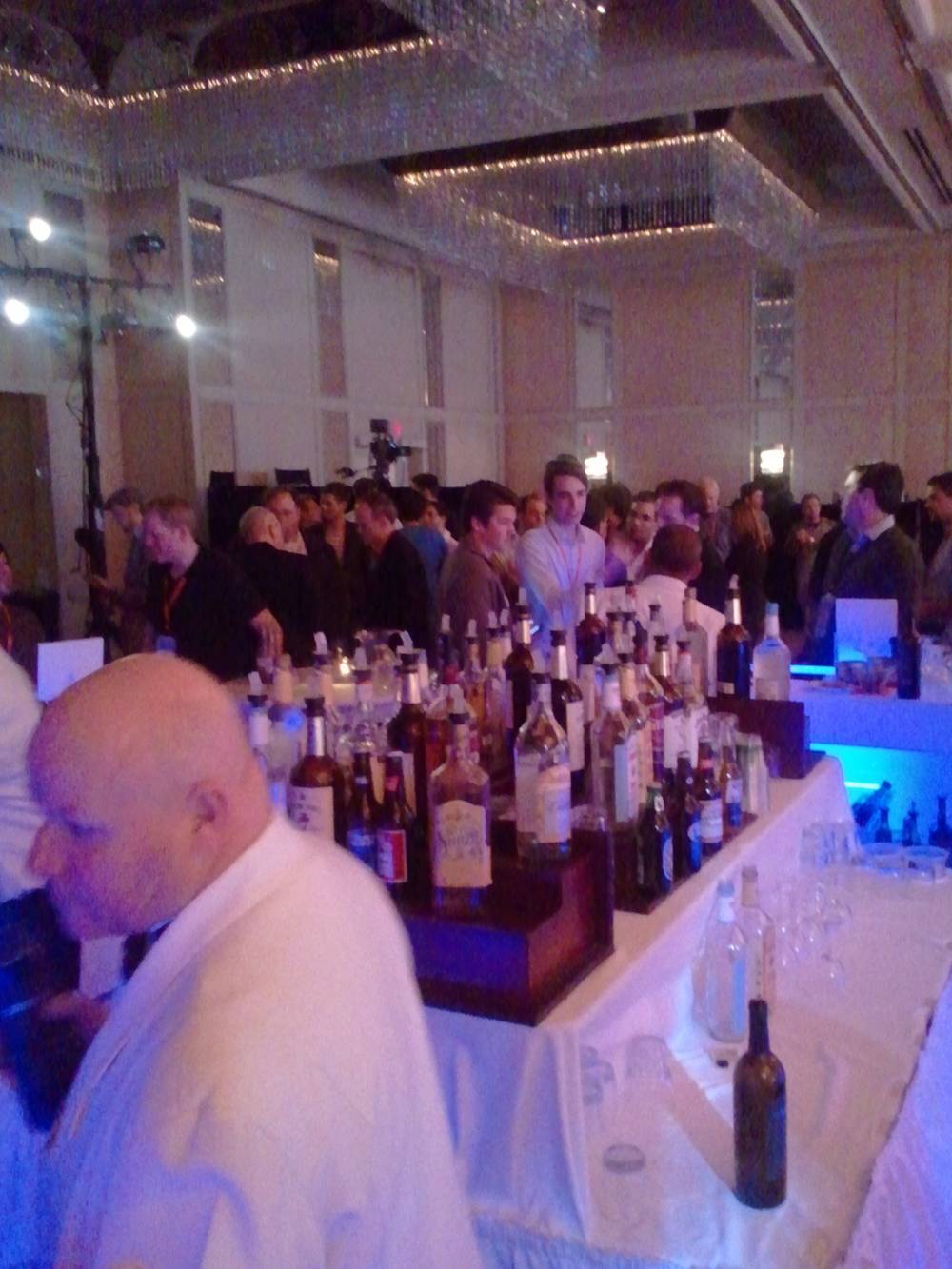 A bartender in a white robe pours drinks for a crowd at an elegant evening reception.