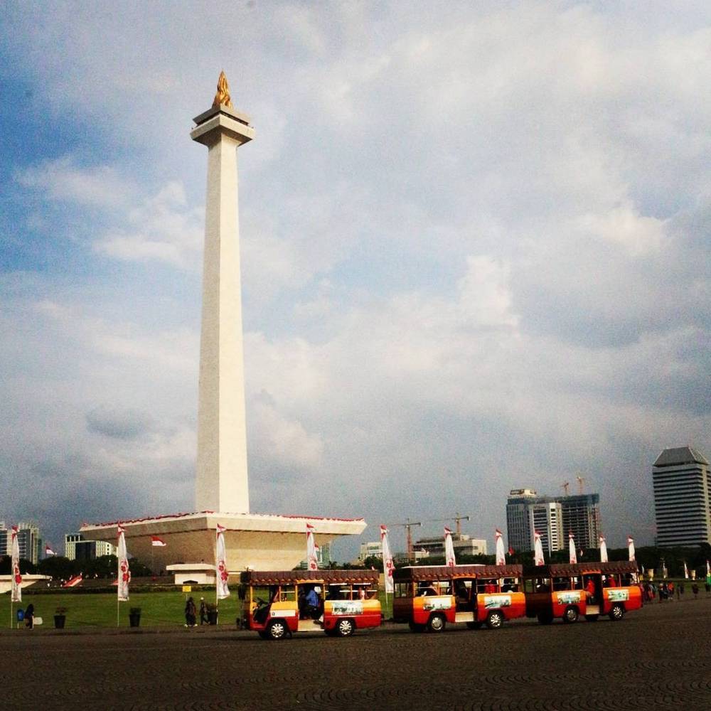 The National Monument obelisk in Jakarta with decorative vehicles parked nearby.