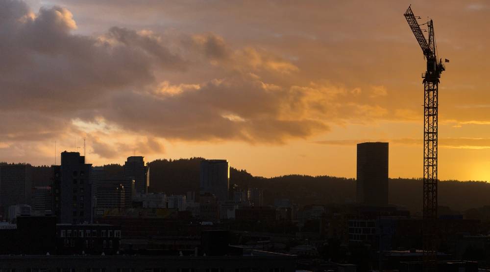 City landscape silhouetted by the sunset. Rolling hills in the background a crane on the right.