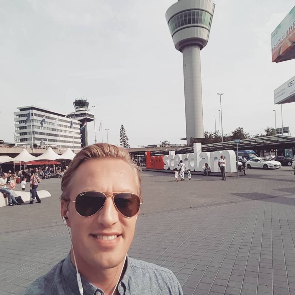 Selfie at Amsterdam Schiphol Airport, with the air traffic control tower visible in the background.
