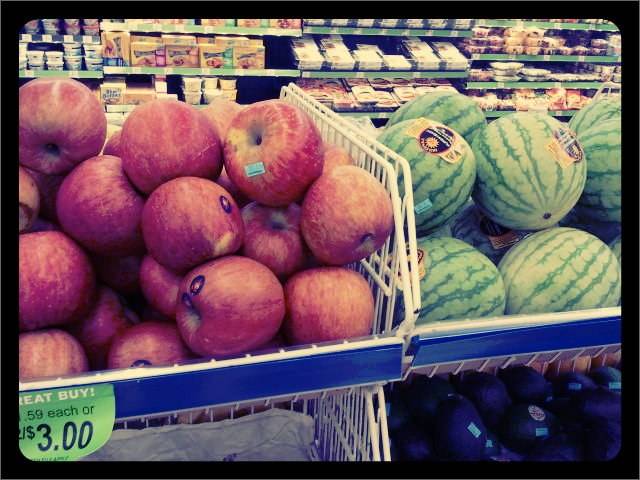 Apples and watermelons are piled on a grocery store display shelf.