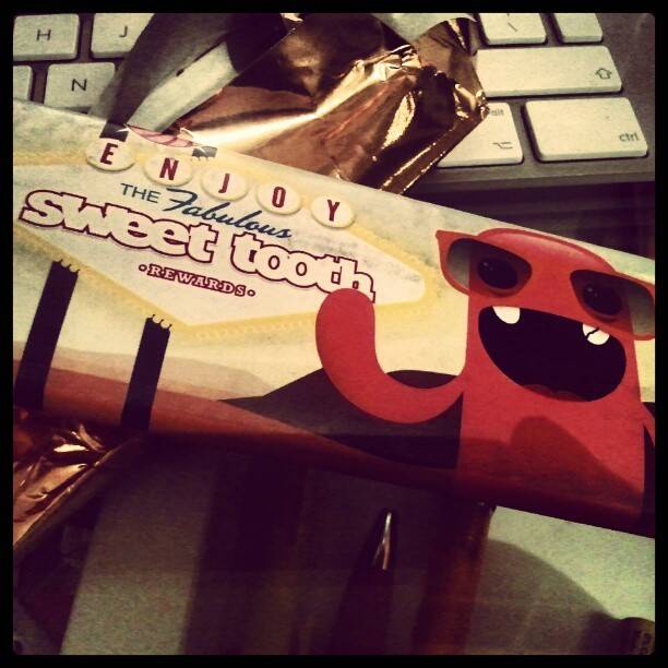 A partly unwrapped chocolate bar reading 'Enjoy the Fabulous Sweet Tooth Rewards' on a keyboard.