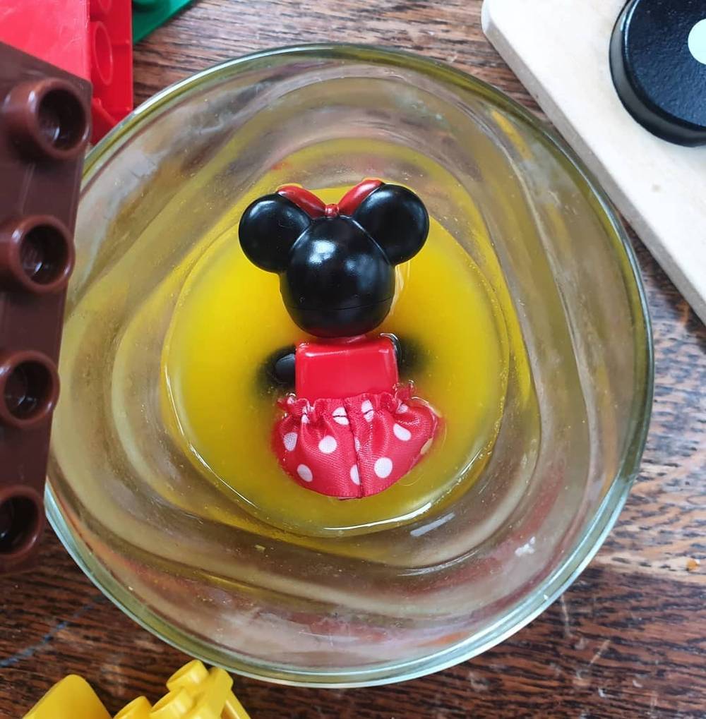 A small Minnie Mouse toy figure floating in a glass of orange juice, seen from above.