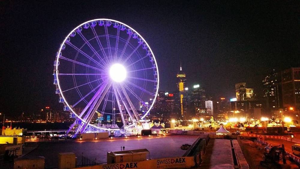 A lit purple Ferris wheel at night against a city skyline reflected on the water.