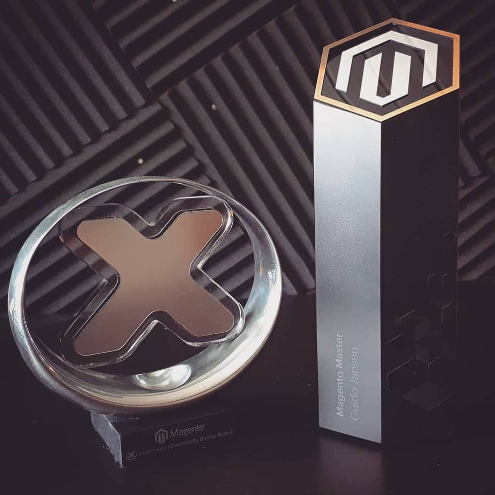 Two glass and metal Magento trophy awards displayed against a dark patterned background.