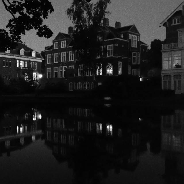 A row of historic townhouses along a dark canal at dusk, reflected in the water.