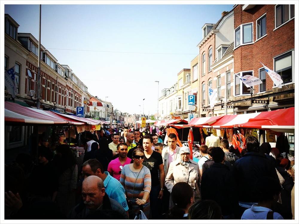 A crowded outdoor market street lined with red-and-white striped stalls and old houses.