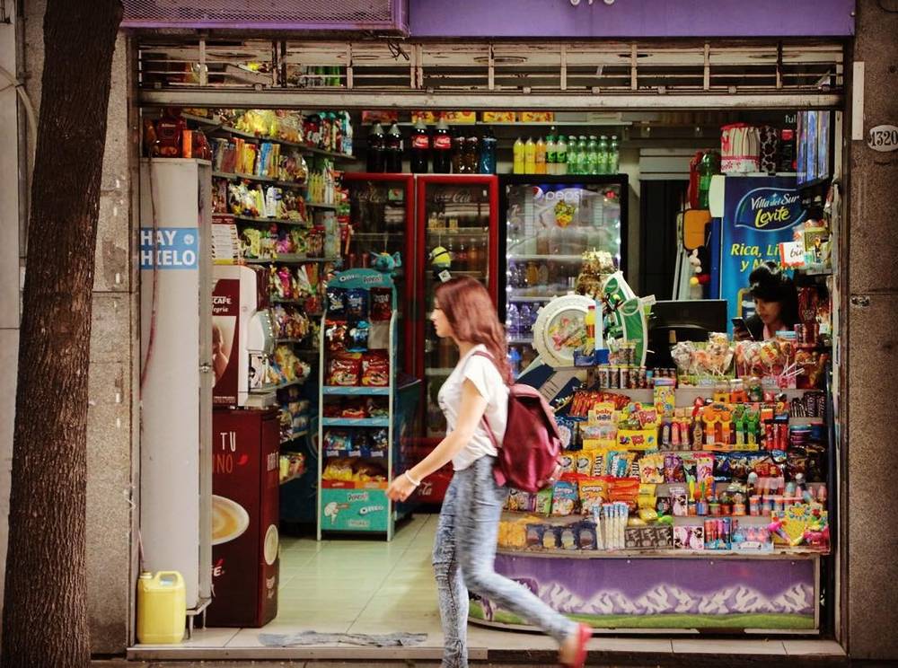 A woman walking past a small convenience kiosk stocked with snacks and drinks.