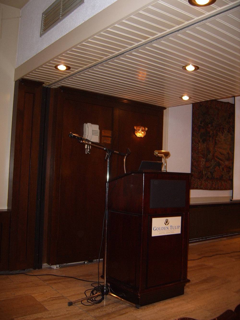 An empty lectern with a "Golden Tulip" sign and microphone waits before a conference session.