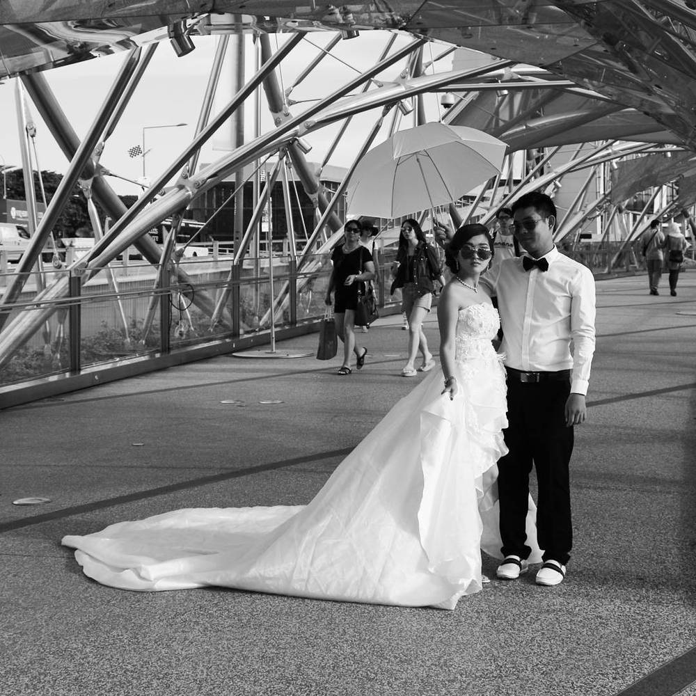 Black and white photo of a bride and groom posing under the Helix Bridge structure.