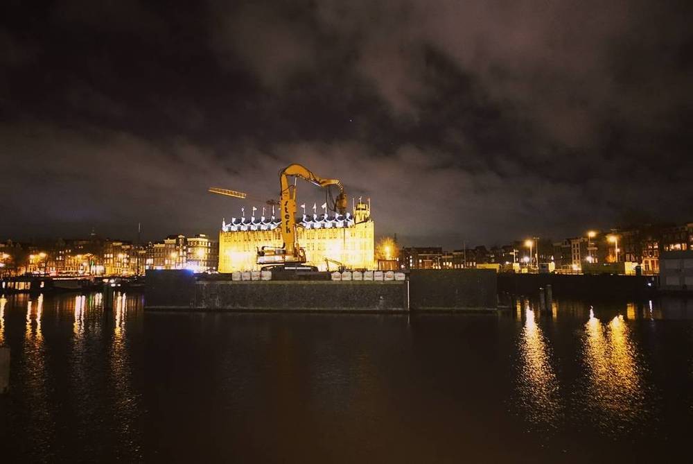 A building under construction, illuminated at night and reflected in the water.