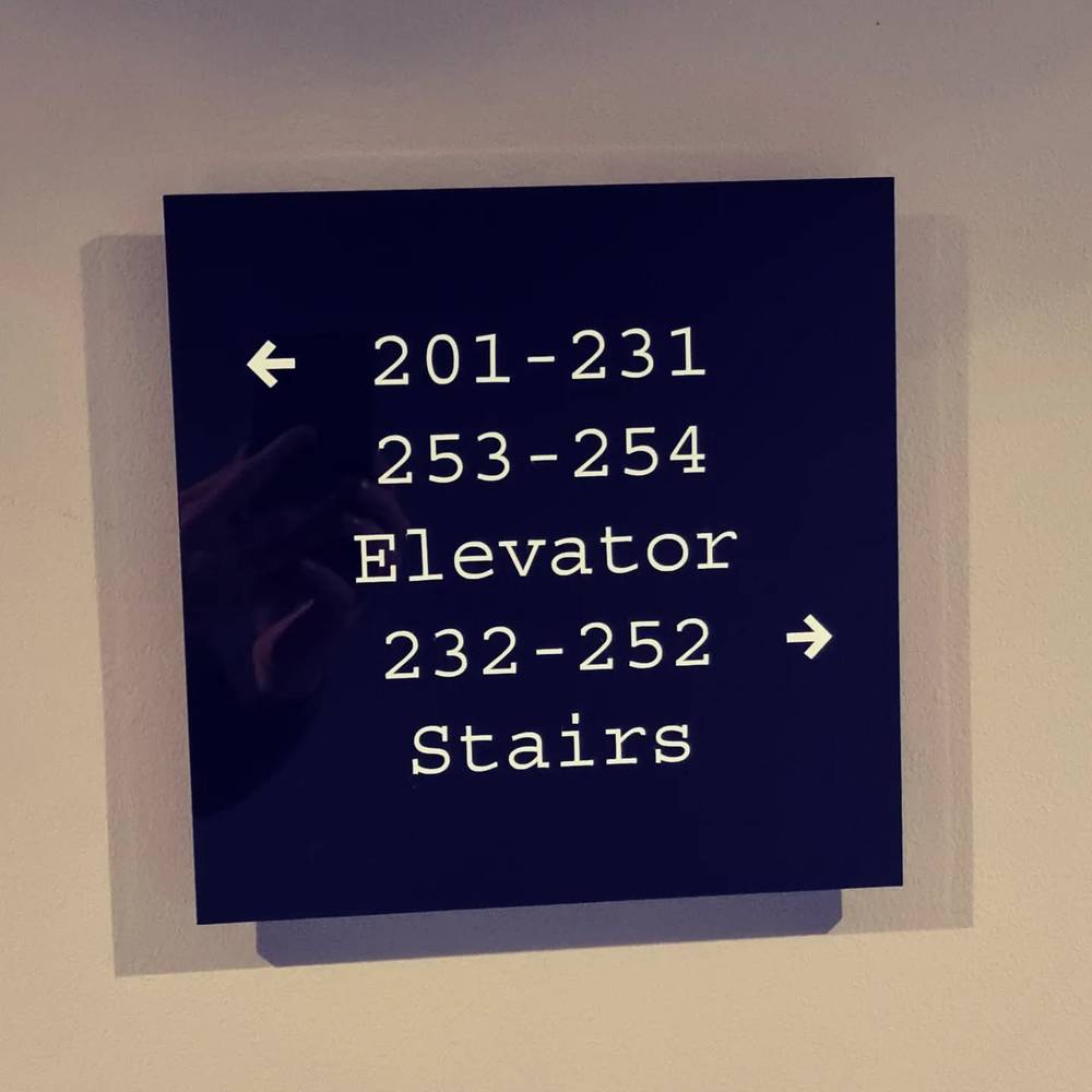 A wall-mounted directional sign listing hotel room number ranges, an elevator, and stairs.