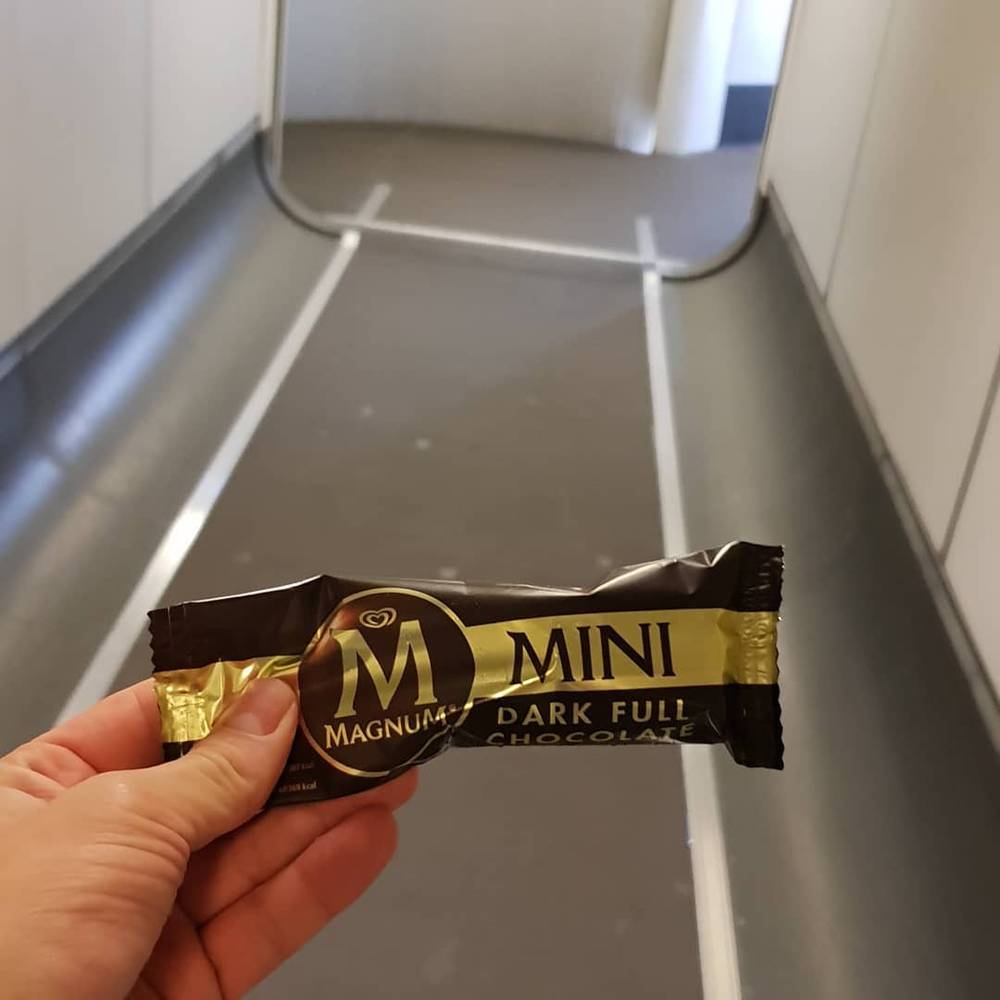 A hand holding a Magnum Mini Dark chocolate ice cream on a plane.