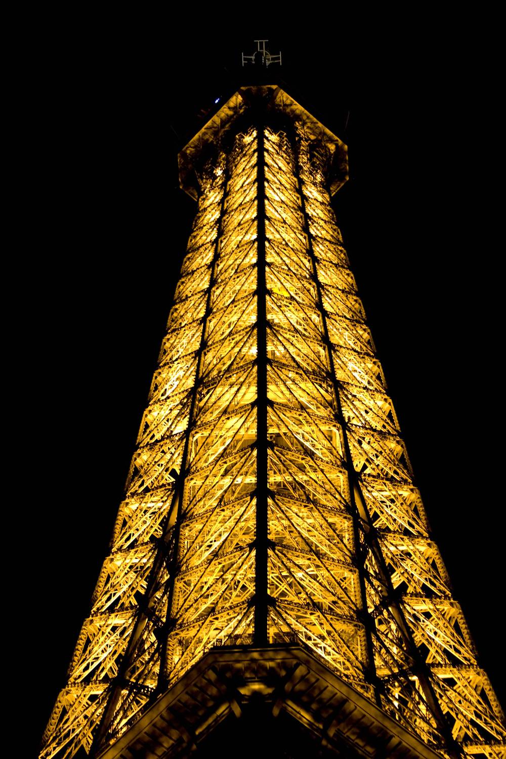 The Eiffel Tower's peak glows gold against the night sky.